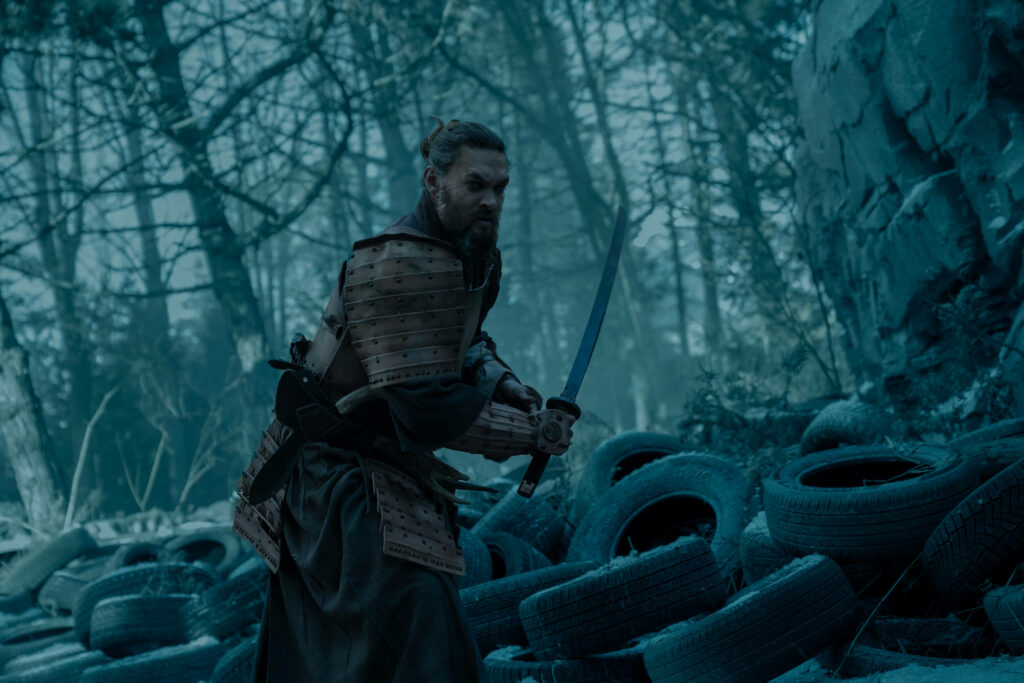 Jason Momoa in armor with sword in misty forest surrounded by scattered tires from See series Wallpaper