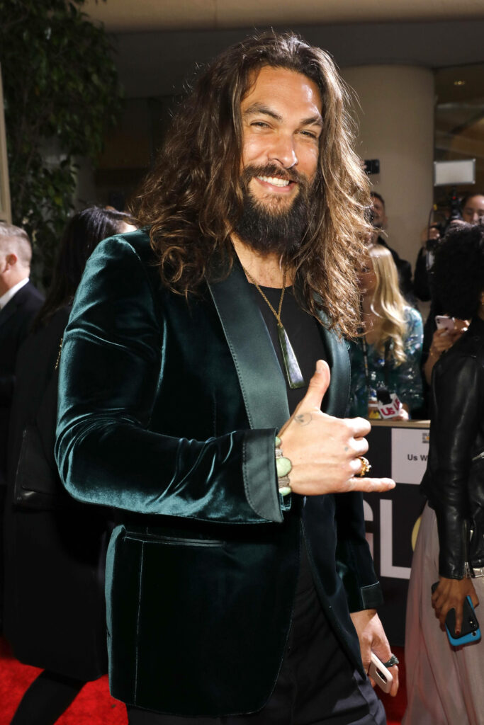 Jason Momoa in dark green velvet suit confident on red carpet wallpaper background