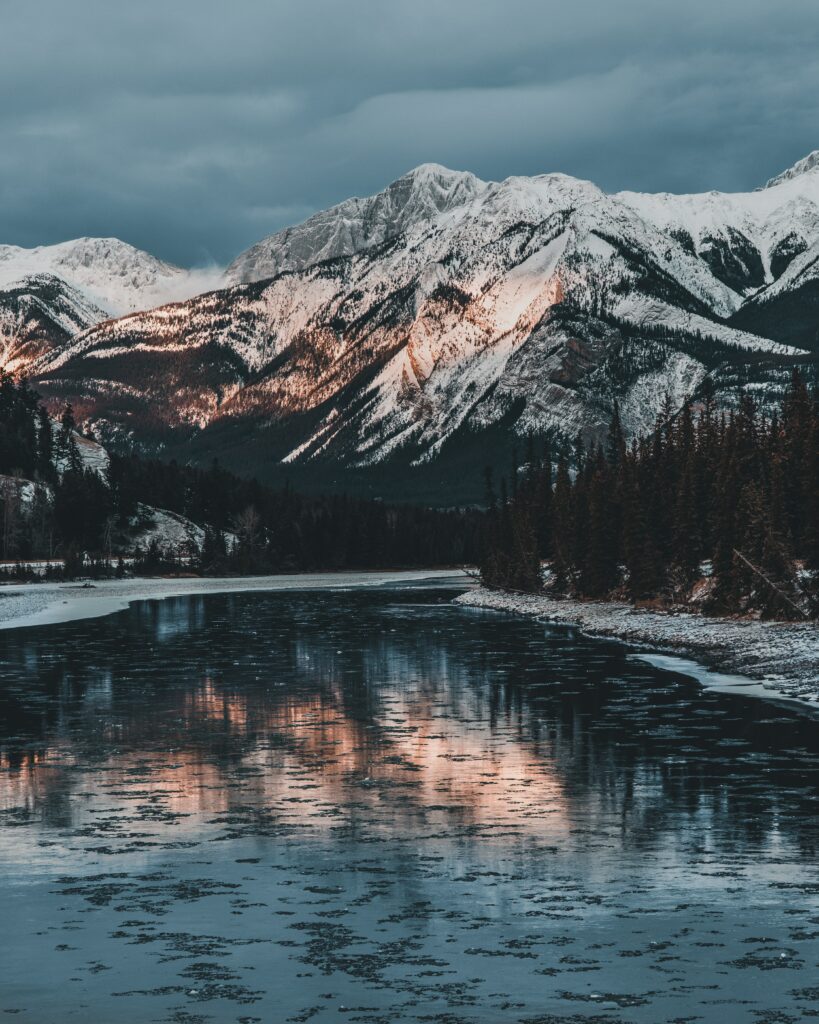 Snow-capped Jasper mountains reflected in a calm lake with snowy slopes and evergreen trees Wallpaper