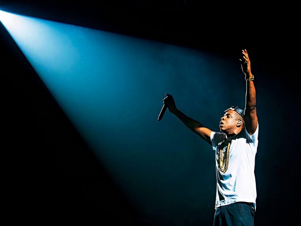 Jay-Z on stage raising arms under bright spotlight creating energetic concert atmosphere wallpaper