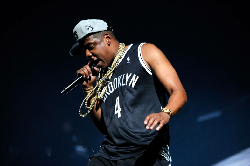 Jay-Z performing live in Brooklyn Nets jersey with gold chains and Brooklyn cap on stage Wallpaper