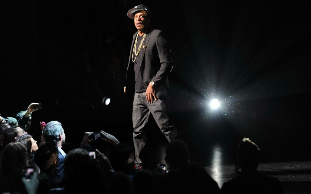 Jay-Z performing on stage in spotlight energizing enthusiastic concert crowd wallpaper background
