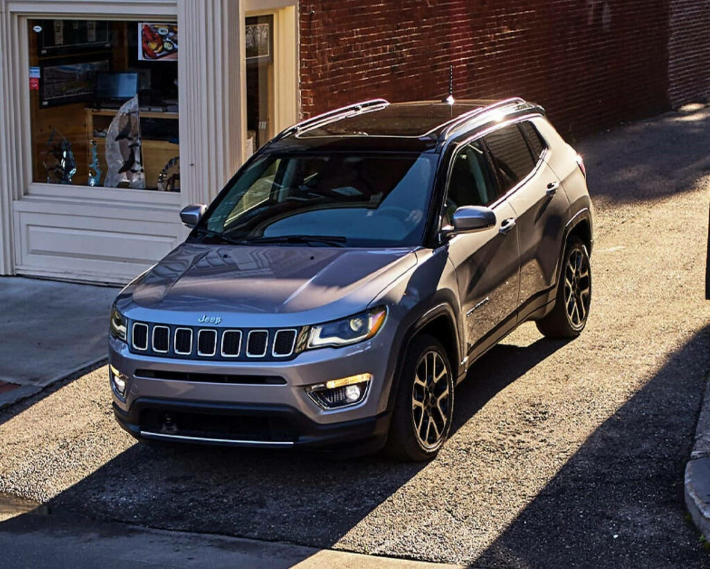 Jeep Compass parked on sunlit road beside brick building showcasing sleek modern design Wallpaper