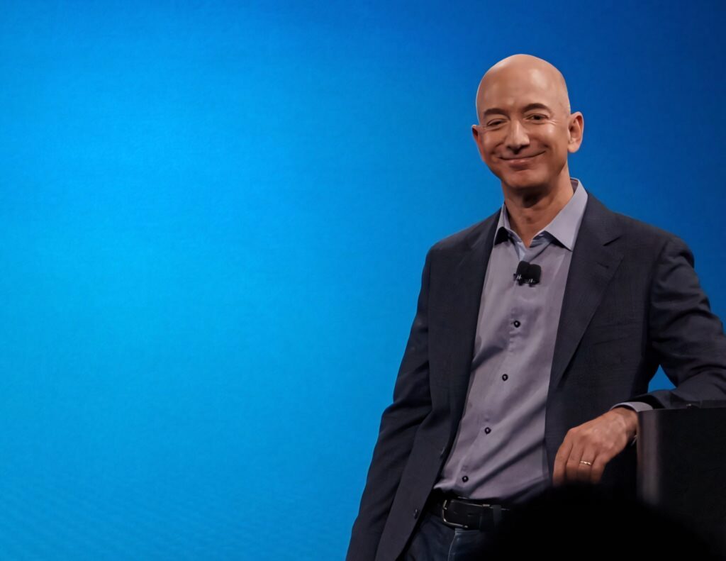 Confident Jeff Bezos Wallpaper: Leaning with a Bright Blue Background