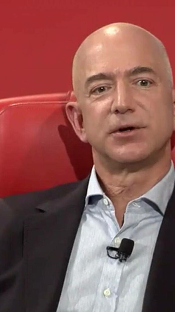 Jeff Bezos Wallpaper: Confident in Suit Against Vibrant Red Background