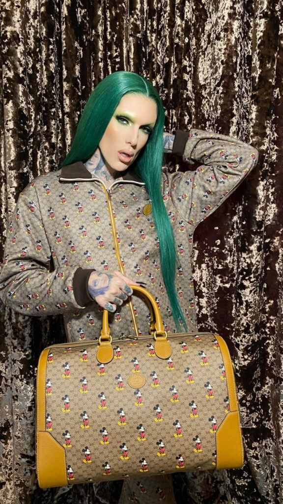 Jeffree Star in designer outfit and luxury handbag against shimmering velvet wallpaper background