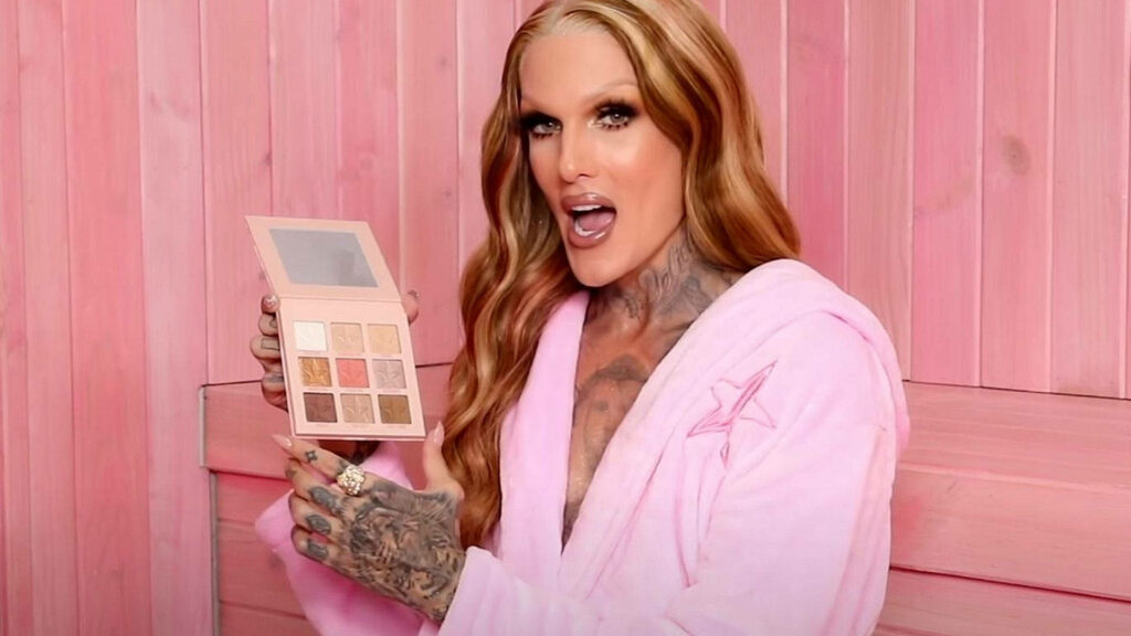 Jeffree Star in pink robe holding mini eyeshadow palette pink wooden background beauty vibe Wallpaper