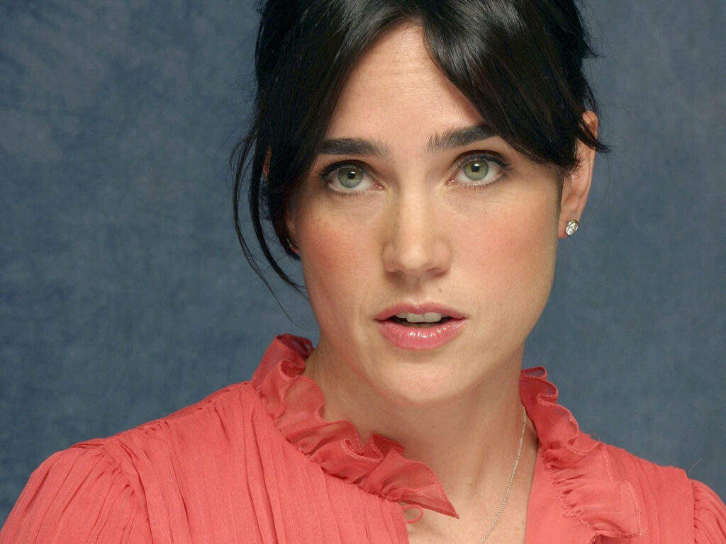 Jennifer Connelly in soft pink ruffle blouse posing naturally against simple blue backdrop Wallpaper