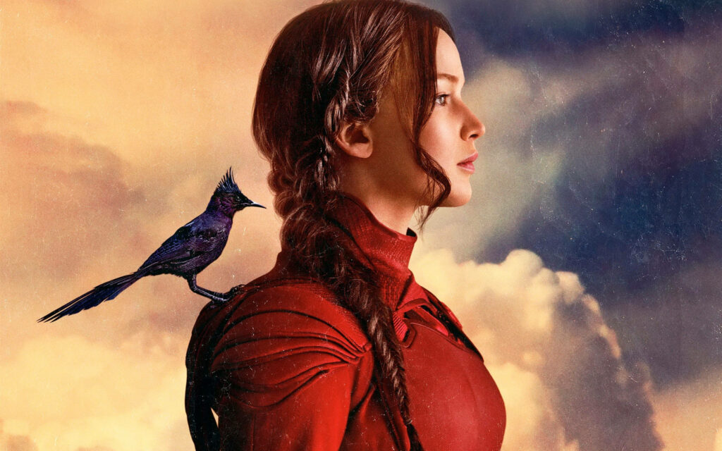 Jennifer Lawrence in profile with black Mockingjay bird on shoulder against dramatic sky background Wallpaper