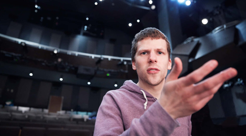 Jesse Eisenberg on theater stage dramatic lighting expressive gesture intense thoughtful moment Wallpaper