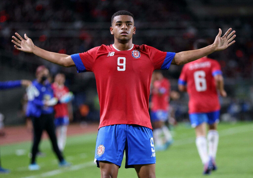 Jewison Bennette in red Costa Rica jersey celebrates on field with teammates and stadium crowd background Wallpaper