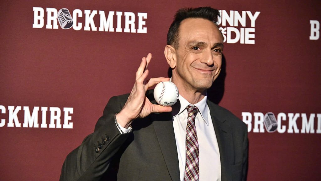 Hank Azaria as Jim Brockmire in suit holding baseball smiling maroon Brockmire backdrop wallpaper