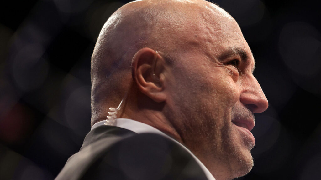 Joe Rogan close up wearing suit and earpiece focused on commentary with wallpaper background