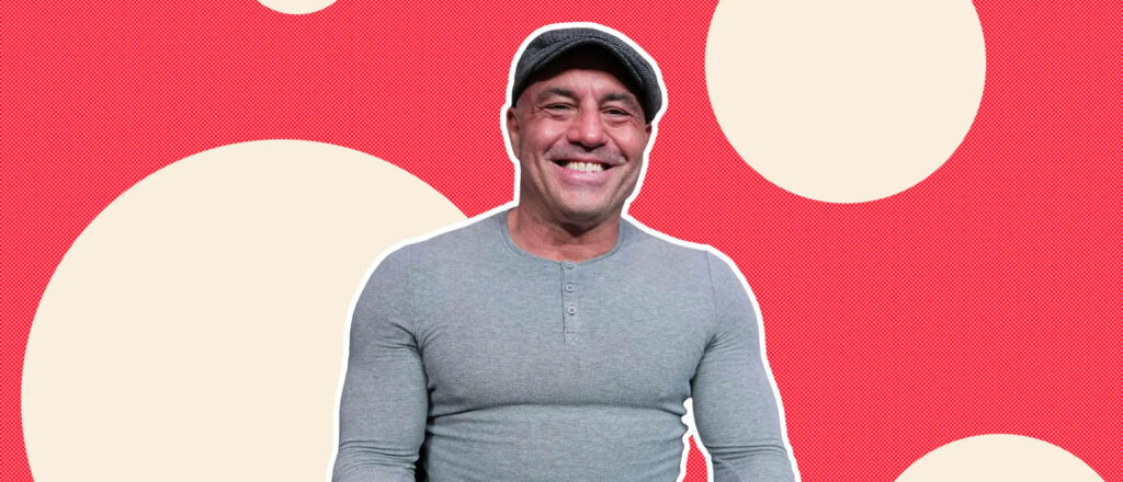 Joe Rogan in tight gray shirt standing against vibrant red wallpaper with cream large circles