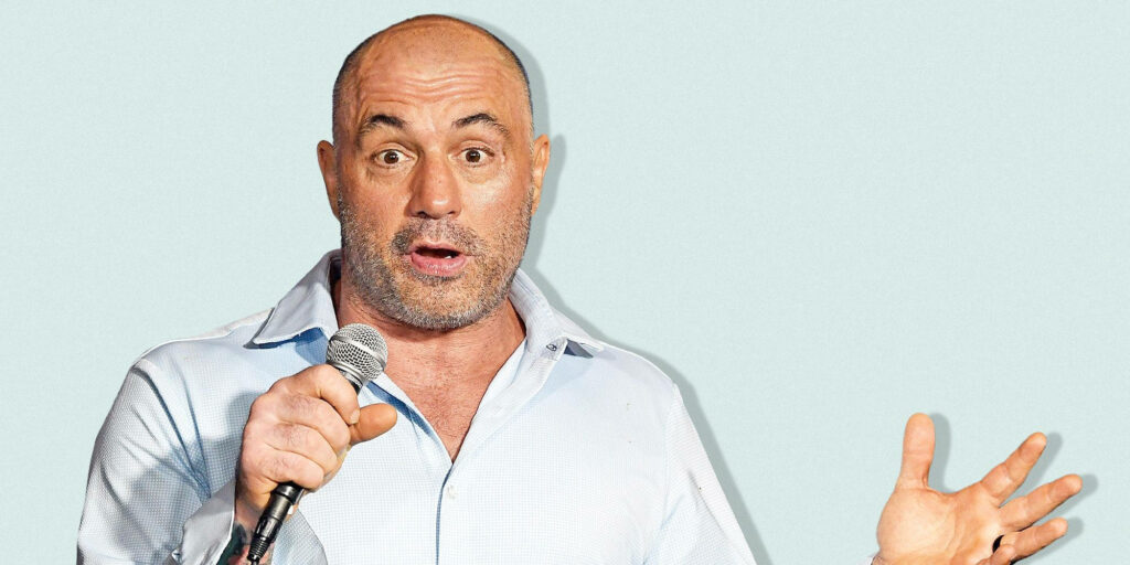 Joe Rogan speaking energetically into microphone wearing light shirt simple wallpaper background