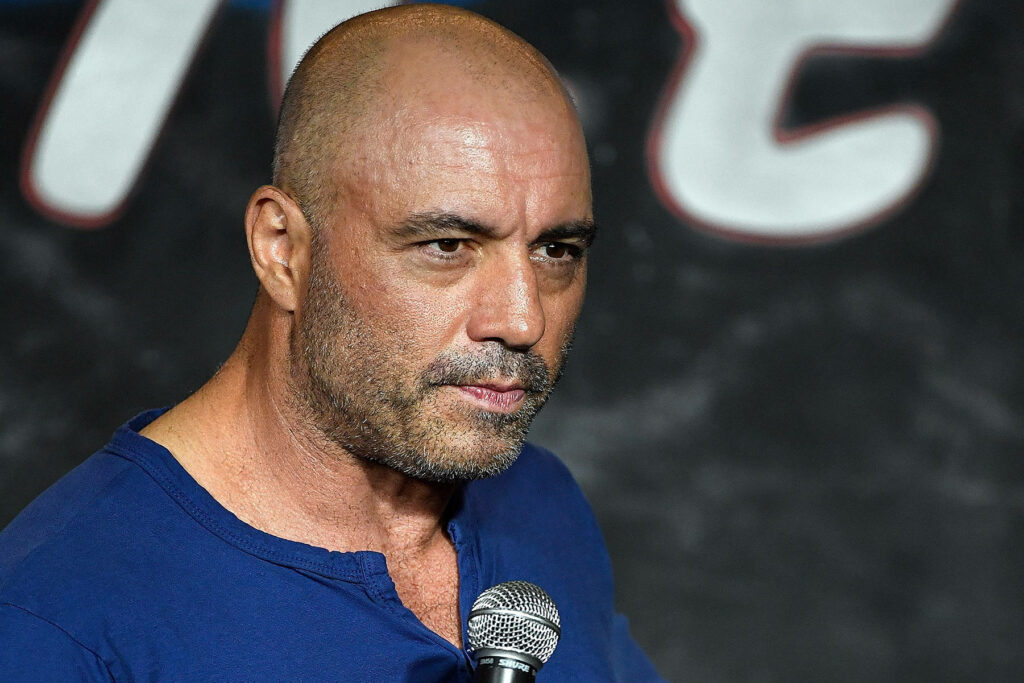 Joe Rogan on stage holding microphone focused during live performance with wallpaper background
