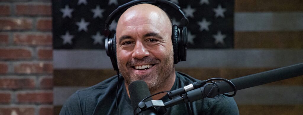 Joe Rogan smiling with headphones and microphone American flag background podcast studio Wallpaper