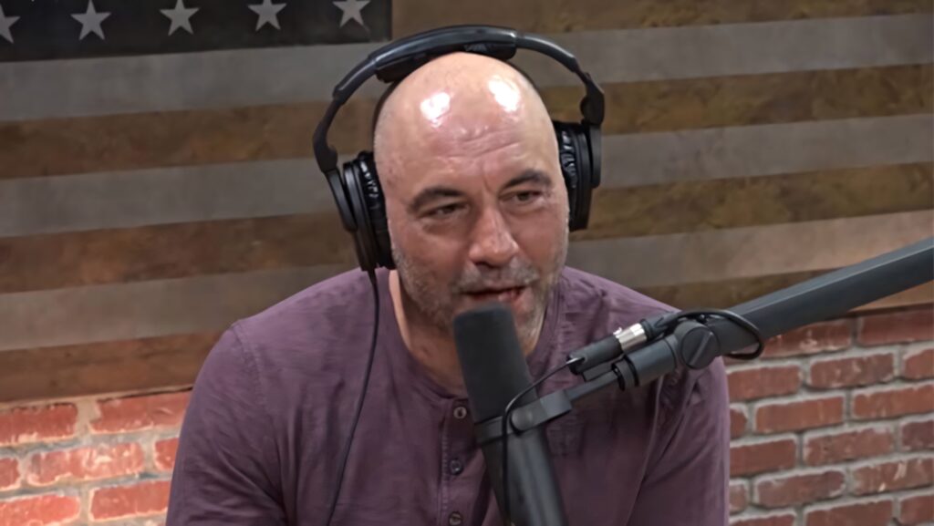 Joe Rogan podcast wallpaper with headphones speaking into mic American flag brick wall background