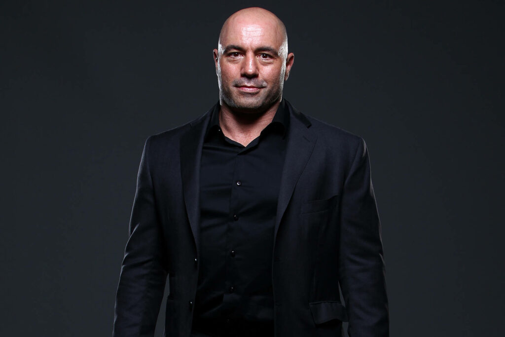 Joe Rogan in dark suit posing confidently against black background sleek professional wallpaper