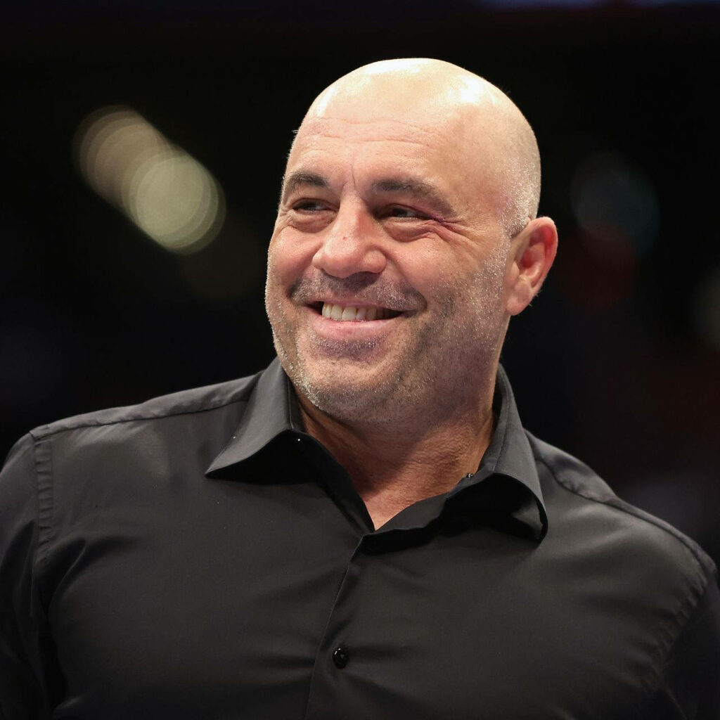 Joe Rogan smiling in black shirt against softly blurred background wallpaper image