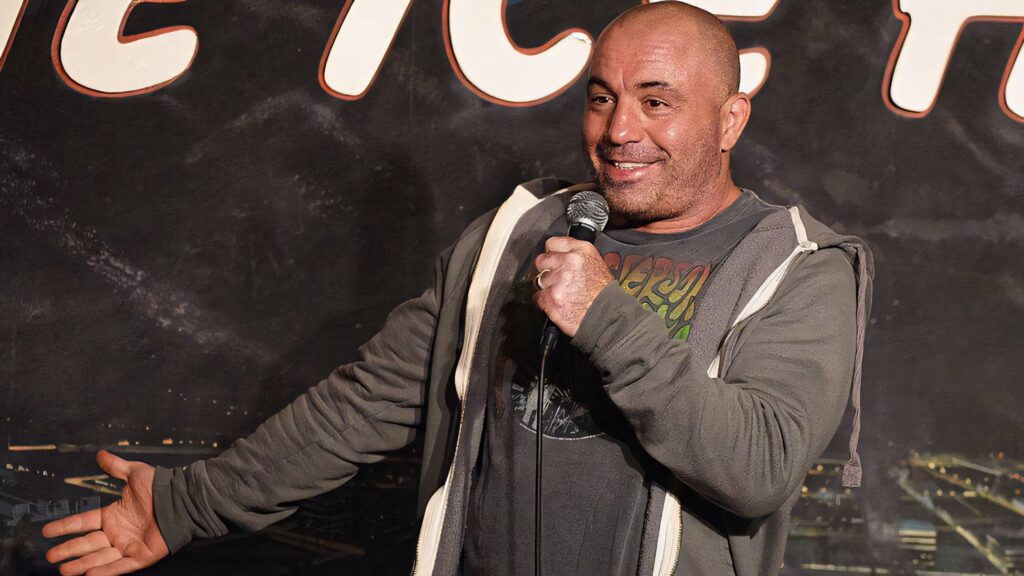 Joe Rogan performing stand-up comedy on stage holding microphone with expressive style wallpaper background