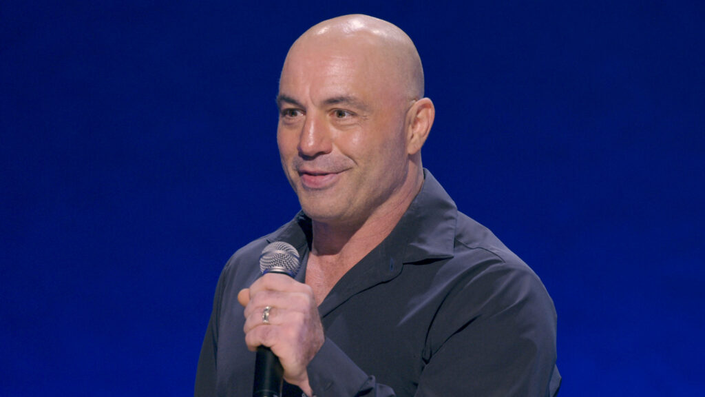 Joe Rogan performing intense stand-up comedy on stage with microphone against blue background Wallpaper