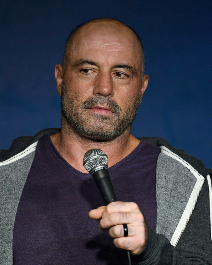 Joe Rogan close-up on stage holding microphone blue background stand-up comedy performance wallpaper