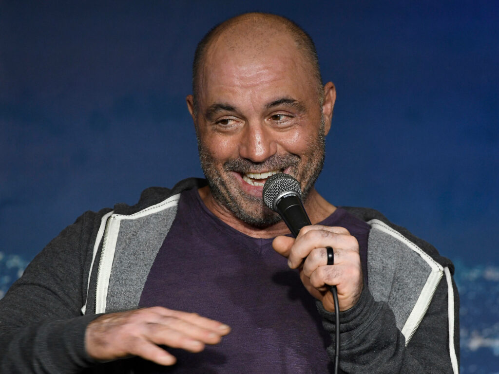 Joe Rogan smiling on stage with microphone during a lively stand-up comedy performance wallpaper