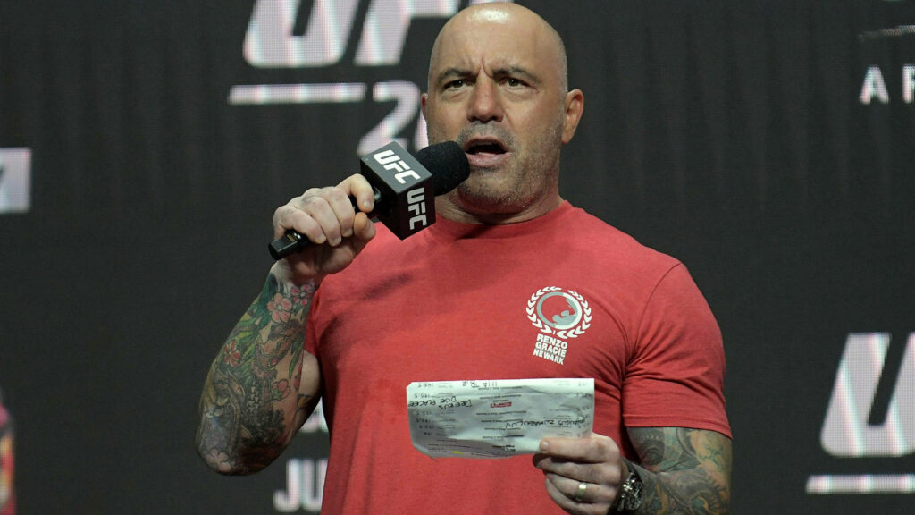 Joe Rogan announcing UFC fighter weights on stage holding microphone and weigh-in card Wallpaper
