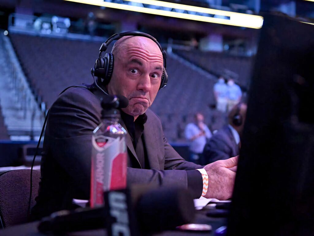 Joe Rogan ringside UFC commentator wearing headphones giving humorous shrug during fight night Wallpaper