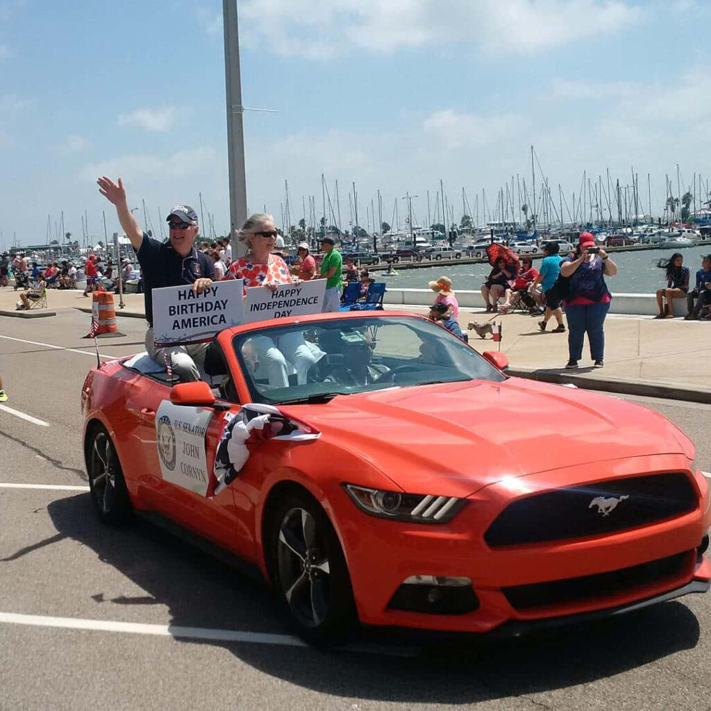 John Cornyn riding bright red convertible at waterfront parade celebrating Americas Independence Day Wallpaper