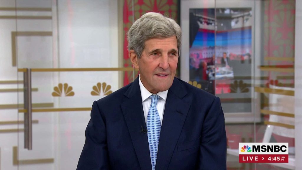 John Kerry in dark suit and blue tie on MSNBC live news broadcast in professional studio setting Wallpaper