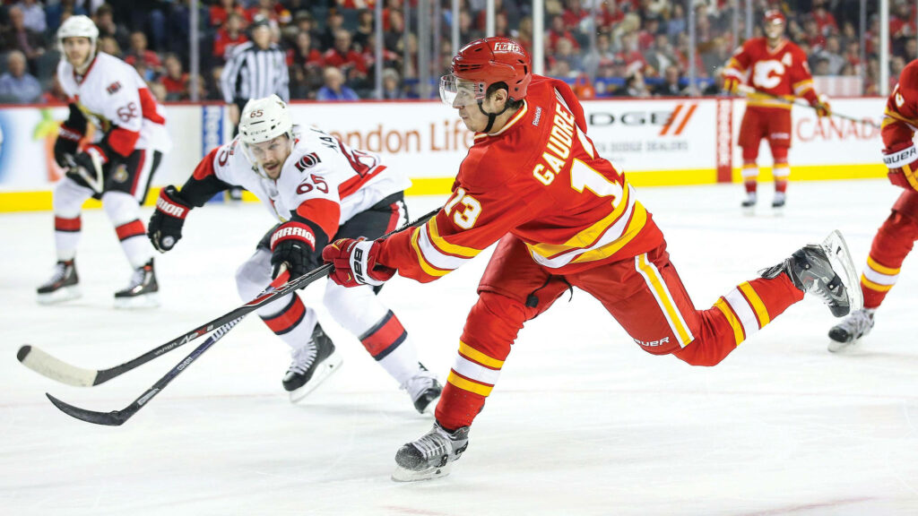 Johnny Gaudreau mid-shot in Calgary Flames jersey intense ice hockey game vibrant arena background Wallpaper