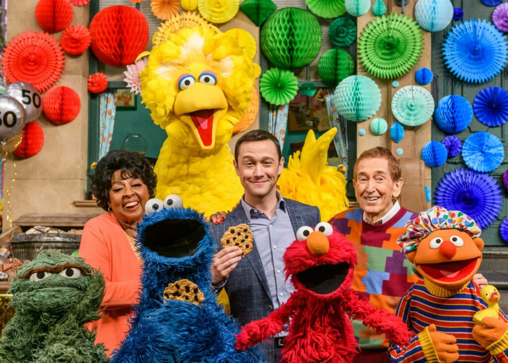 Joseph Gordon-Levitt with Sesame Street characters and cast in colorful festive celebration background Wallpaper