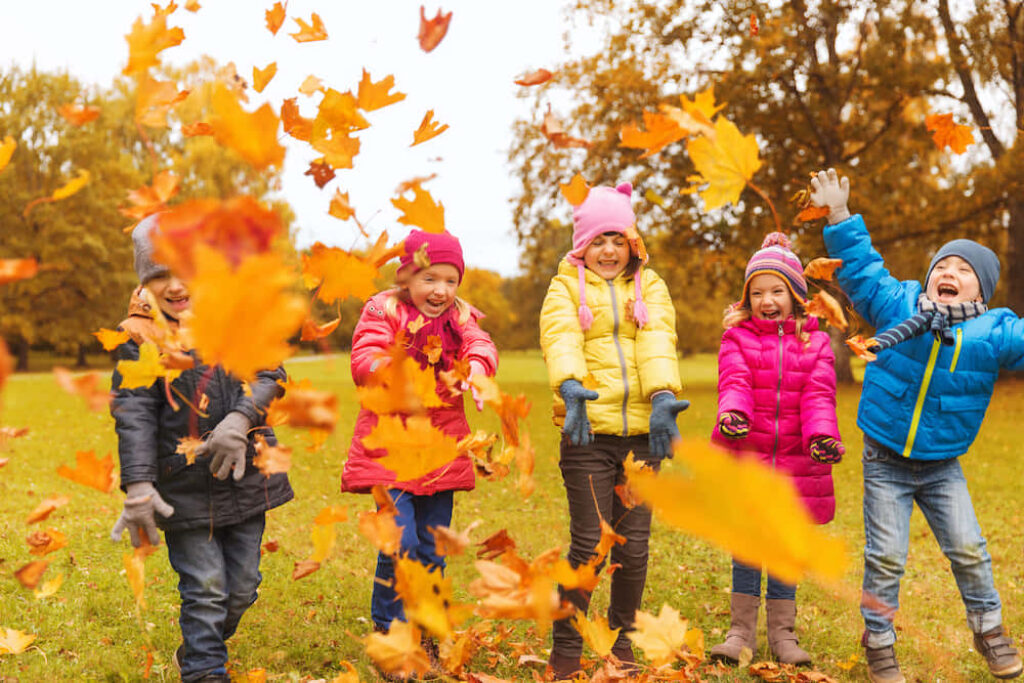 Joyful Autumn Wallpaper: Kids Tossing Colorful Leaves in Vibrant Trees