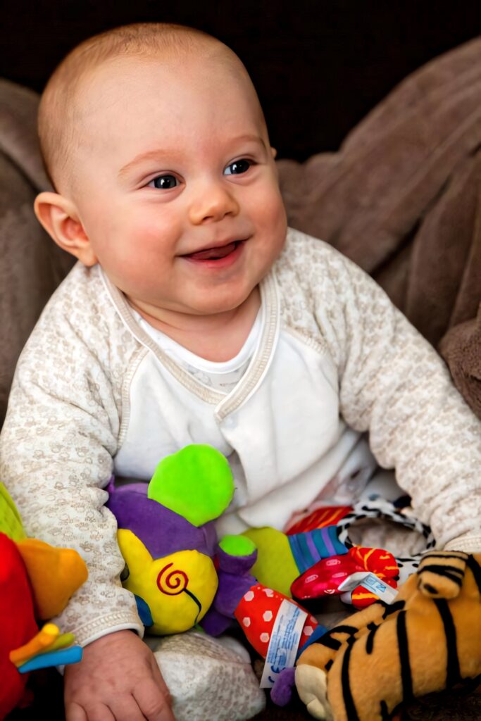 Happy baby boy smiling surrounded by colorful toys cheerful wallpaper background for kids