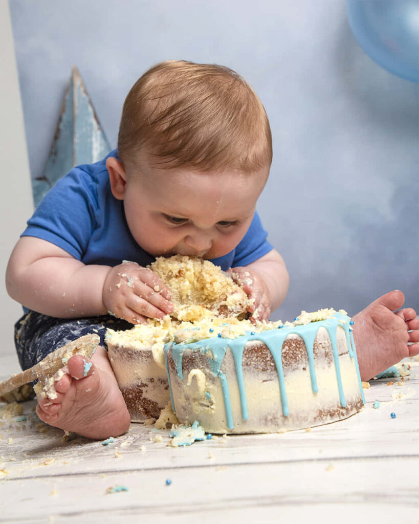 Baby Joyfully Digs into Blue Icing Cake: Adorable Cake Smash Scene Wallpaper