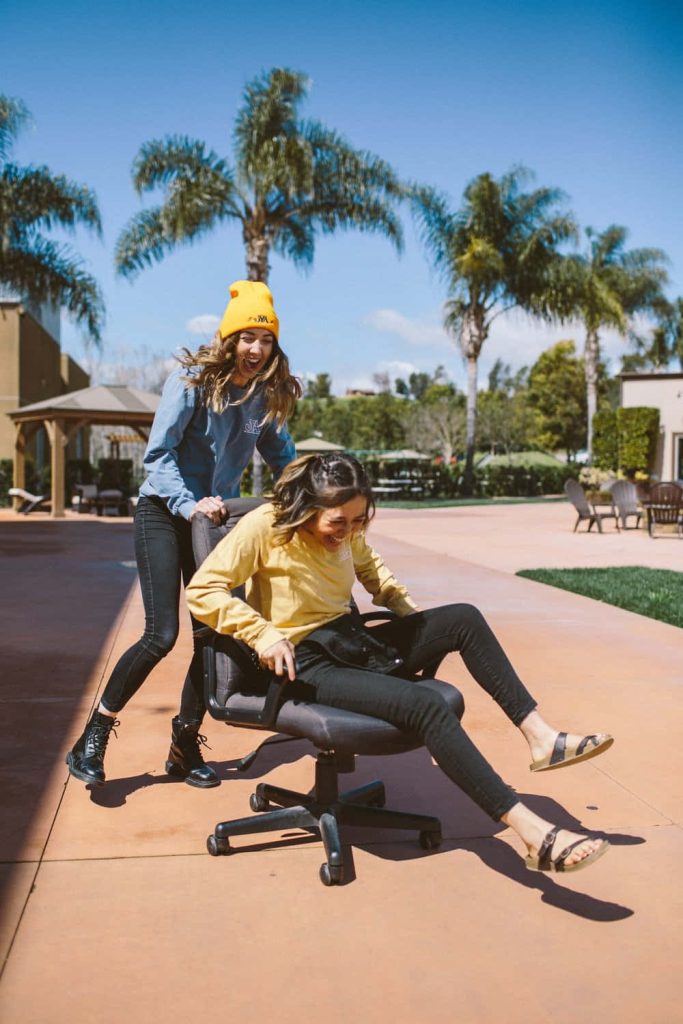 Two best friends laughing and having fun outdoors with one pushing the other in an office chair Wallpaper