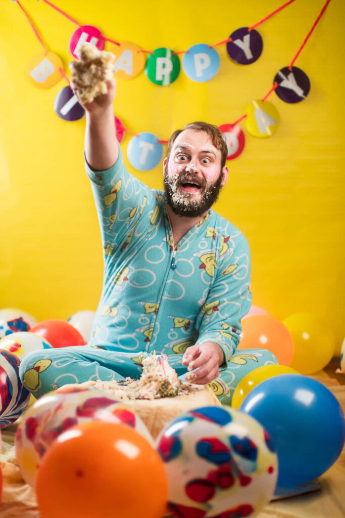 Joyful Birthday Celebration: Man in Colorful PJs Surrounded by Balloons Wallpaper