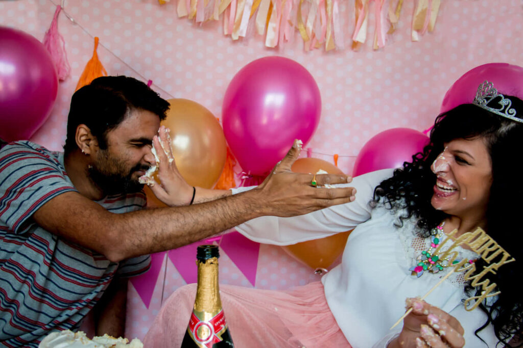 Joyful Cake Smash Celebration: A Couple's Fun with Balloons & Laughter Wallpaper