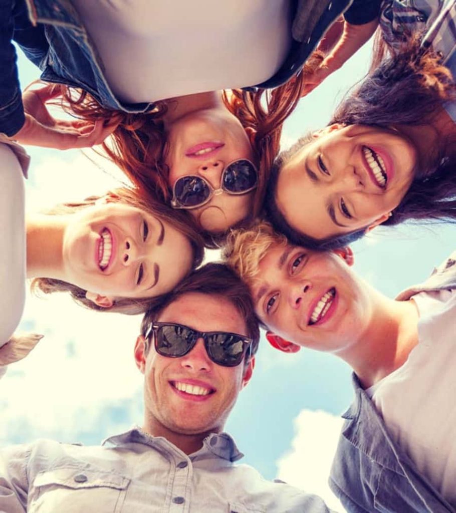 Smiling friends huddled in a circle under bright sunny sky joyful group celebration wallpaper