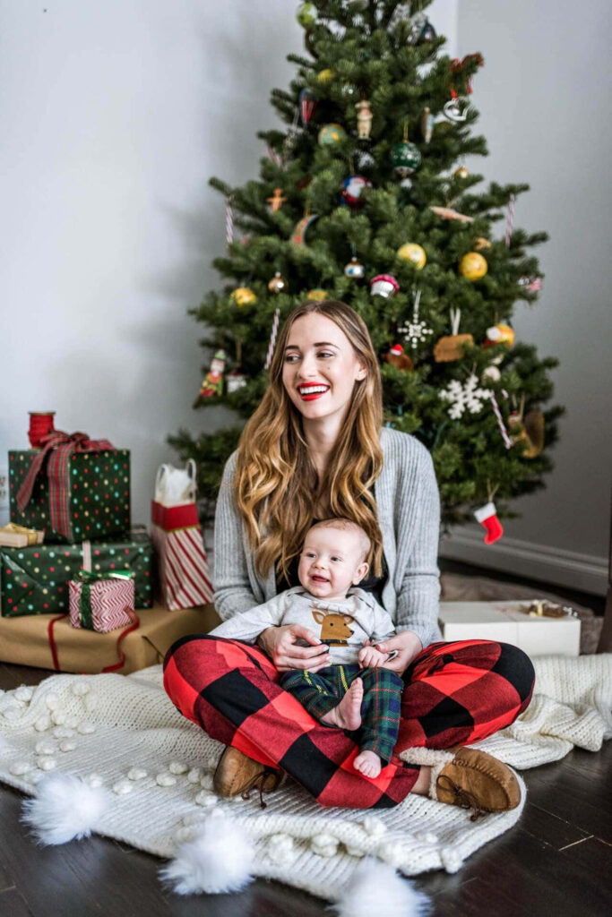 Joyful Holiday Scene: Smiling Mom and Baby by Christmas Tree Wallpaper