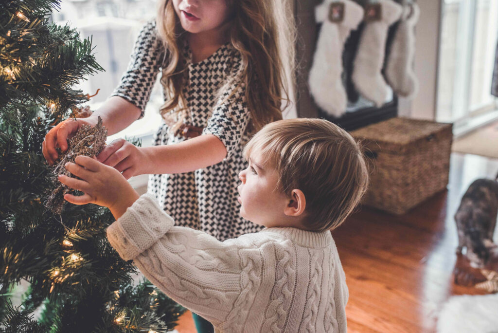 Cozy Christmas Scene: Children Decorating Tree by Festive Fireplace Wallpaper