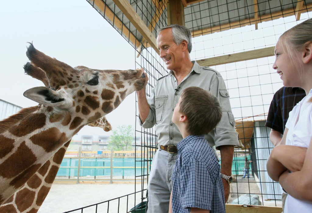 Joyful Connection: Man and Giraffe at Zoo with Children Watching Wallpaper