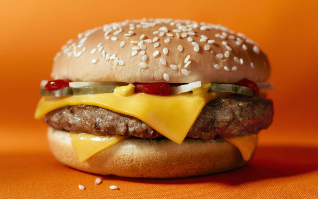 Juicy Cheeseburger Close-Up with Cheese & Pickles on Orange Wallpaper