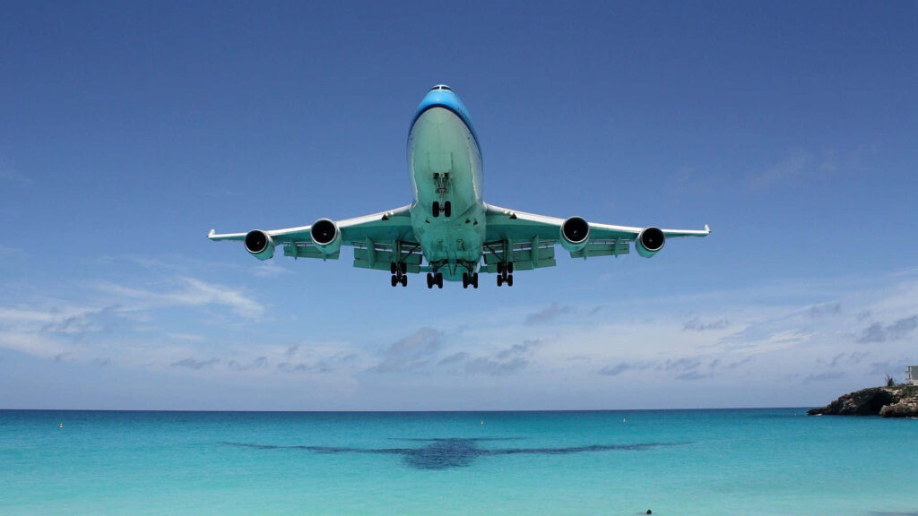 A Spectacular Aerial Venture: Majestic Jumbo Jet Carrying Passengers Over Serene Blue Skies Wallpaper