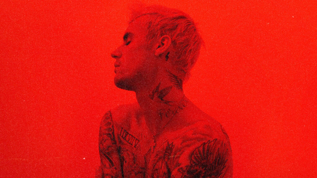 Justin Bieber in red wallpaper showing tattoos and relaxed reflective pose 2021 vibe