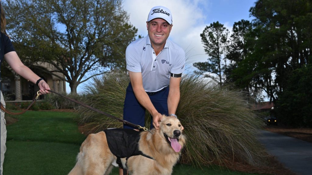 Justin Thomas smiling with friendly Golden Retriever outdoors in sunny lush green golf setting Wallpaper