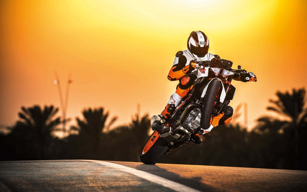 Vibrant KTM Motorcycle Wheelie Wallpaper at Sunset | Scenic Adventure