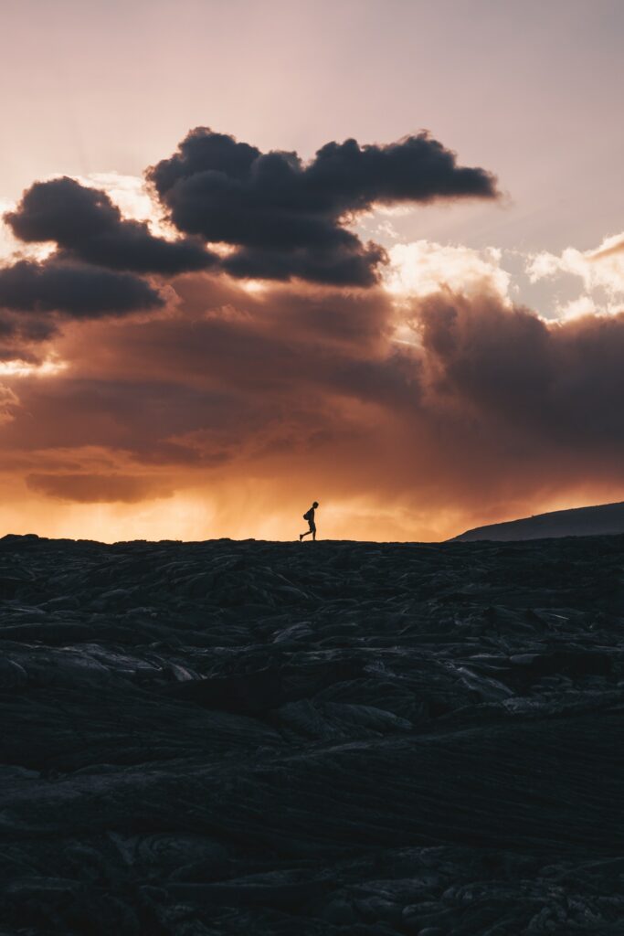 Silhouette on rugged volcanic terrain Kalapana Hawaii sunset glowing orange purple clouds wallpaper